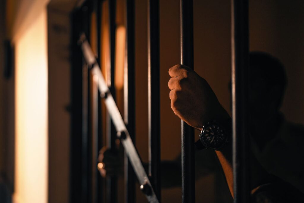 Silhouetted hand gripping jail bars, highlighting solitude and confinement.